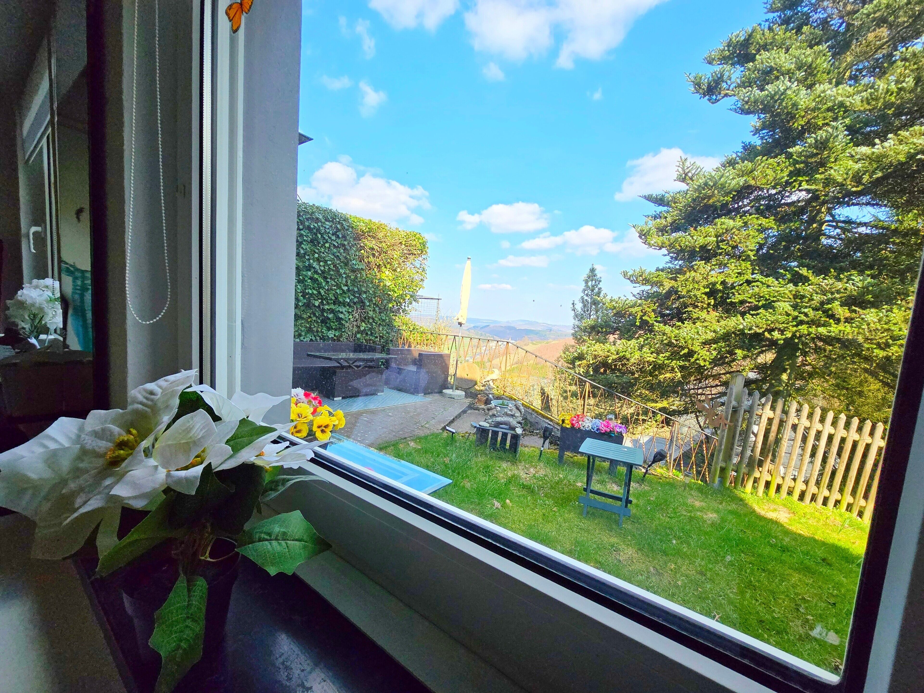 A view through a window of a garden with a wooden fence, a bench, and a stone wall.