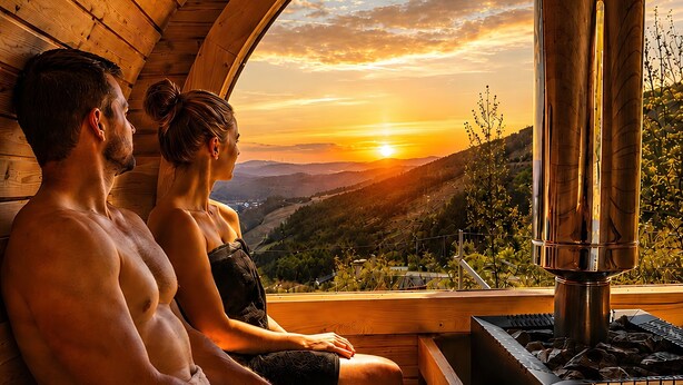 Una cabaña de madera con sauna, vistas al atardecer y una terraza de madera.