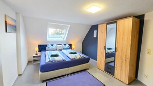 Un dormitorio con cama, ventana, armario y mesita de noche pequeña.