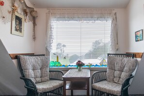 A room with two upholstered chairs, a small table, and a window with a view of a lighthouse and sailboat.