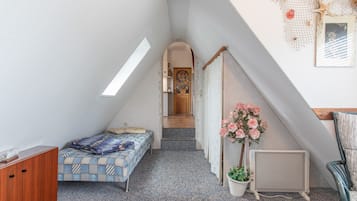 Un dormitorio compacto con techo inclinado, una cama con ropa de cama estampada, una planta en maceta, un radiador y un pequeño armario de madera.
