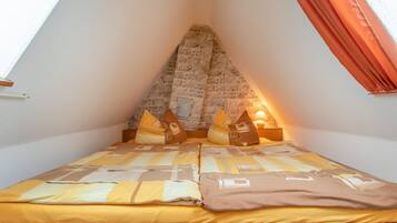 Une chambre avec un plafond en pente, un lit recouvert d’une couvre-lit à motifs et un mur en pierre.