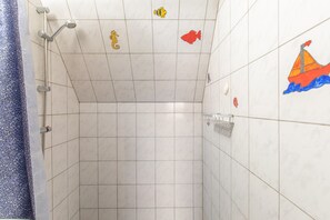 Área de duche com azulejos, chuveiro, porta-toalhas e azulejos decorativos com tema de peixes na parede.