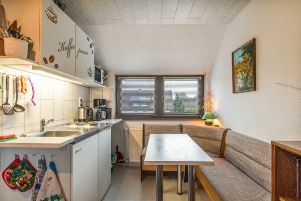 Une cuisine de taille réduite comprenant un coin repas, un radiateur et une fenêtre avec des stores.