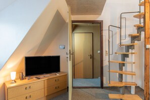 A room with a television on a wooden dresser, a door leading to another room, and a wooden spiral staircase.