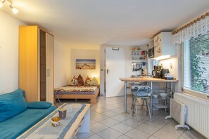 Un espace de vie compact comprenant un coin cuisine, un lit avec une literie à motifs floraux, un canapé bleu et une table à manger agrémentée d’une bougie.