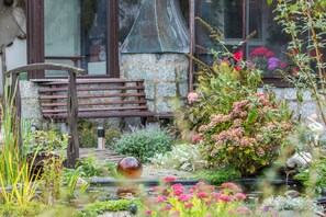 Un banc en pierre, un petit étang et diverses plantes dans un jardin.