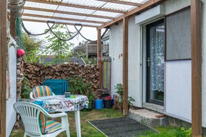 A covered outdoor seating area with a table and chairs, a stone wall, and a wooden pergola.