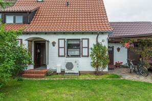 Une maison avec un toit recouvert de tuiles rouges, une porte d’entrée et un petit jardin où se trouve un vélo.