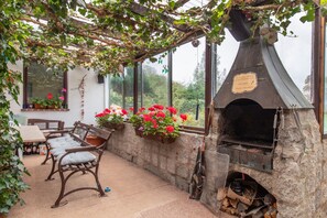 An outdoor patio with a stone barbecue grill, wooden furniture, and potted plants.