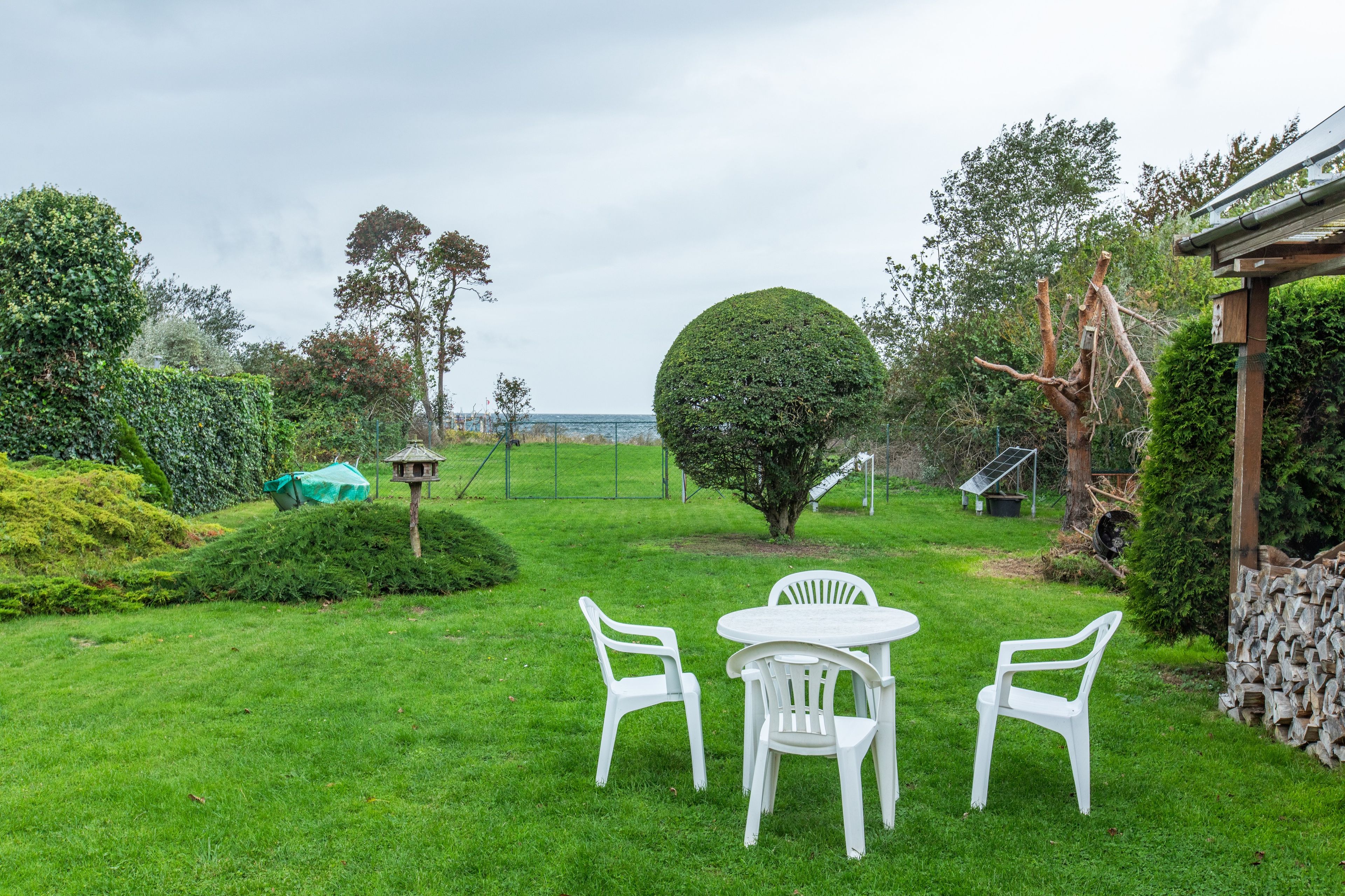 A grassy outdoor area with a round table and two chairs, surrounded by trees and a fence.