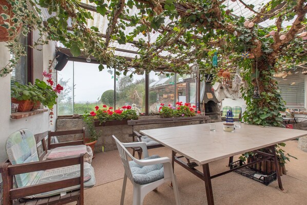 Une terrasse couverte avec une table et des chaises, entourée de plantes et de fleurs en pot.