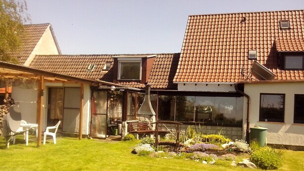 A house with a tiled roof, a patio with chairs, and a garden with various plants. - Studio Apartment 'Ferienwohnungen Hiddenseeblick 3' with Sea View, Shared Terrace and Wi-Fi (Dranske)