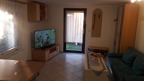 A living room with a television, a sofa, a coffee table, and a door leading outside. - Studio Apartment 'Ferienwohnungen Hiddenseeblick 3' with Sea View, Shared Terrace and Wi-Fi (Dranske)