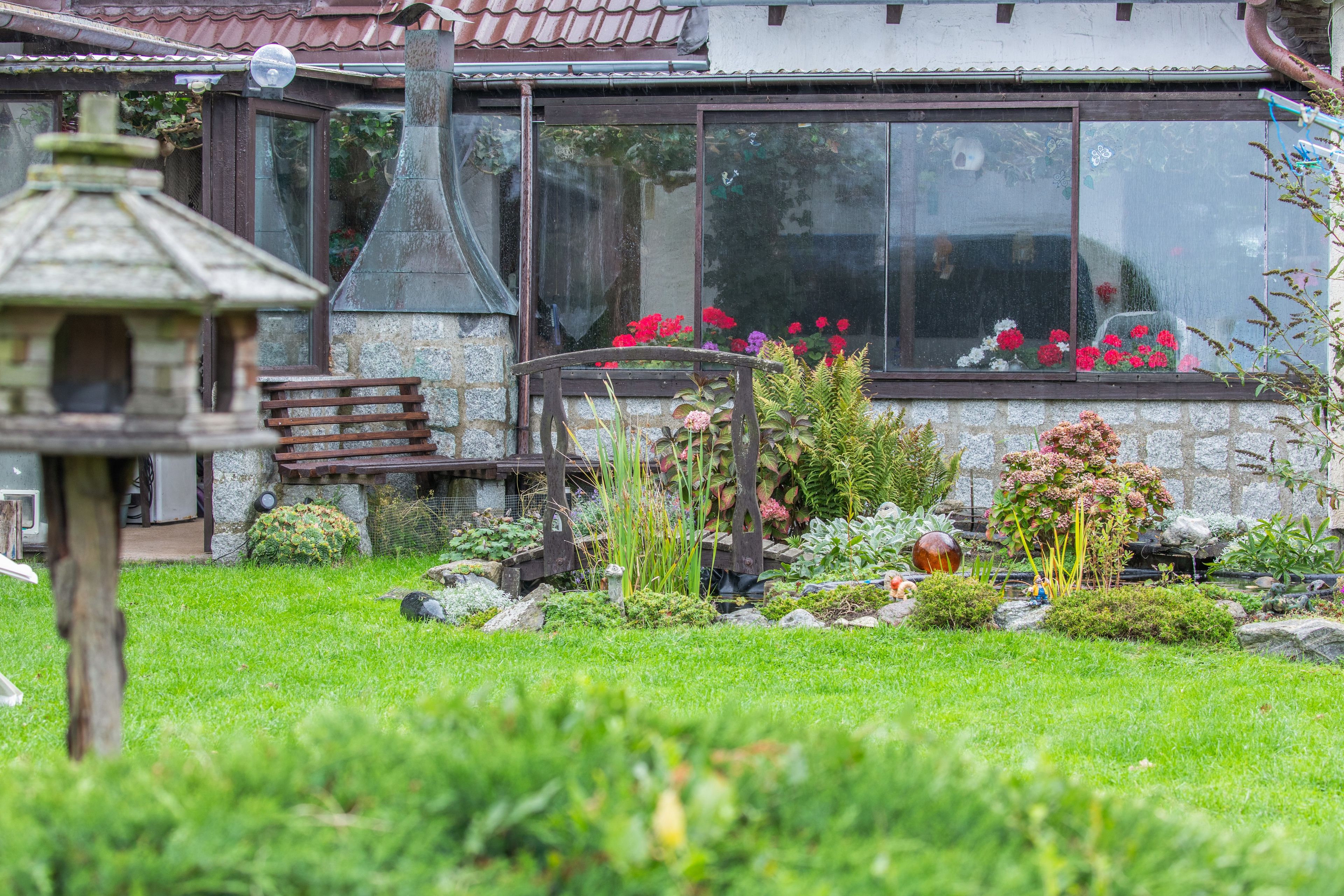 A garden with a wooden bench, a bird feeder, and a variety of plants and flowers.