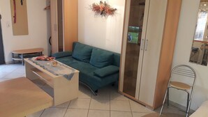 A living room with a green sofa, a small table with a candle, and a metal chair. - Studio Apartment 'Ferienwohnungen Hiddenseeblick 3' with Sea View, Shared Terrace and Wi-Fi (Dranske)