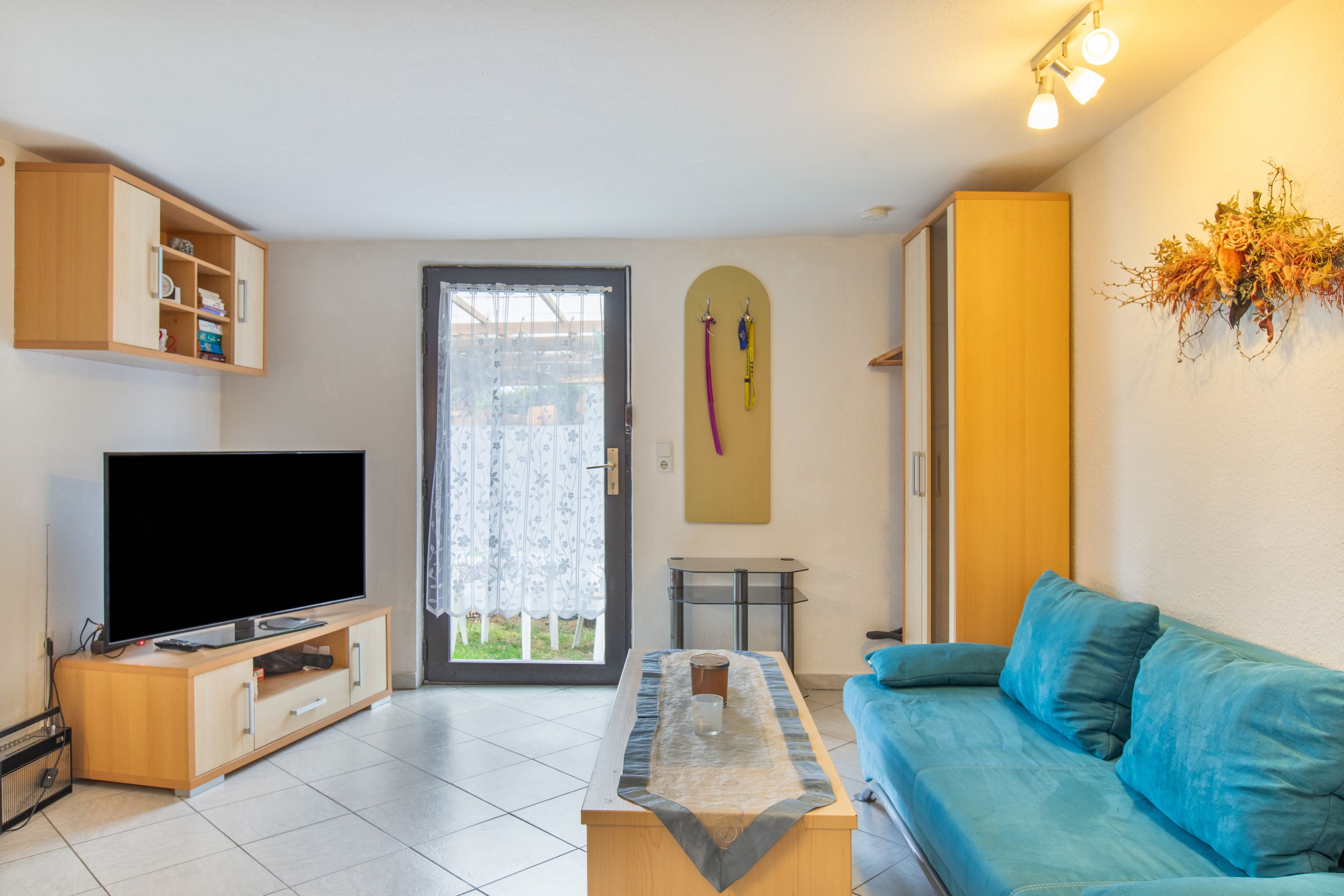 Una sala de estar con un televisor de pantalla plana, un sofá, una mesa de centro, una puerta con cortina y un perchero para esquíes montado en la pared.
