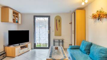 A living room with a flat-screen TV, a sofa, a coffee table, a door with a curtain, and a wall-mounted ski rack.