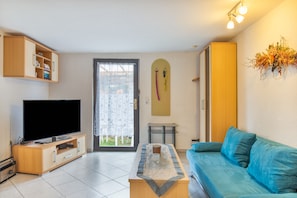 Un salon équipé d’un téléviseur à écran plat, d’un canapé, d’une table basse, d’une porte avec un rideau et d’un porte-skis fixé au mur.