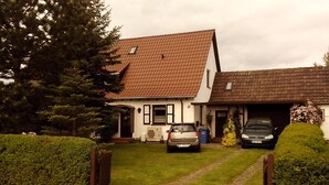 A two-story house with a tiled roof, a garage, and a paved driveway. - Studio Apartment 'Ferienwohnungen Hiddenseeblick 3' with Sea View, Shared Terrace and Wi-Fi (Dranske)