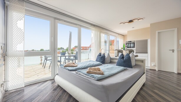 Ein modernes Zimmer mit einem großen Bett, einem Balkon mit Blick und einer Küchenzeile.