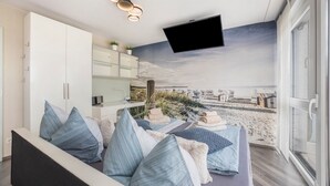 Ein modernes Schlafzimmer mit Bett, Fernseher, Kleiderschrank und Blick auf den Strand.