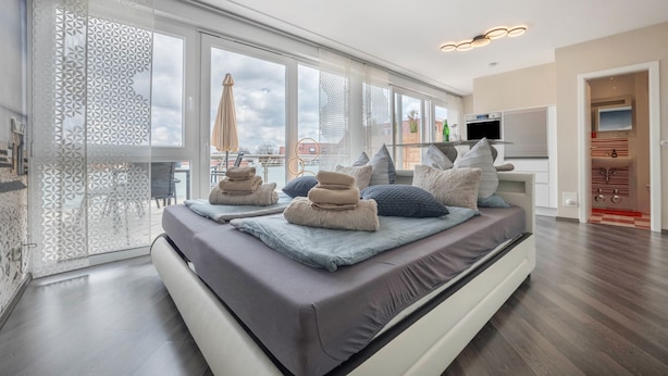A modern bedroom with a large bed, a TV, and a view of the city.