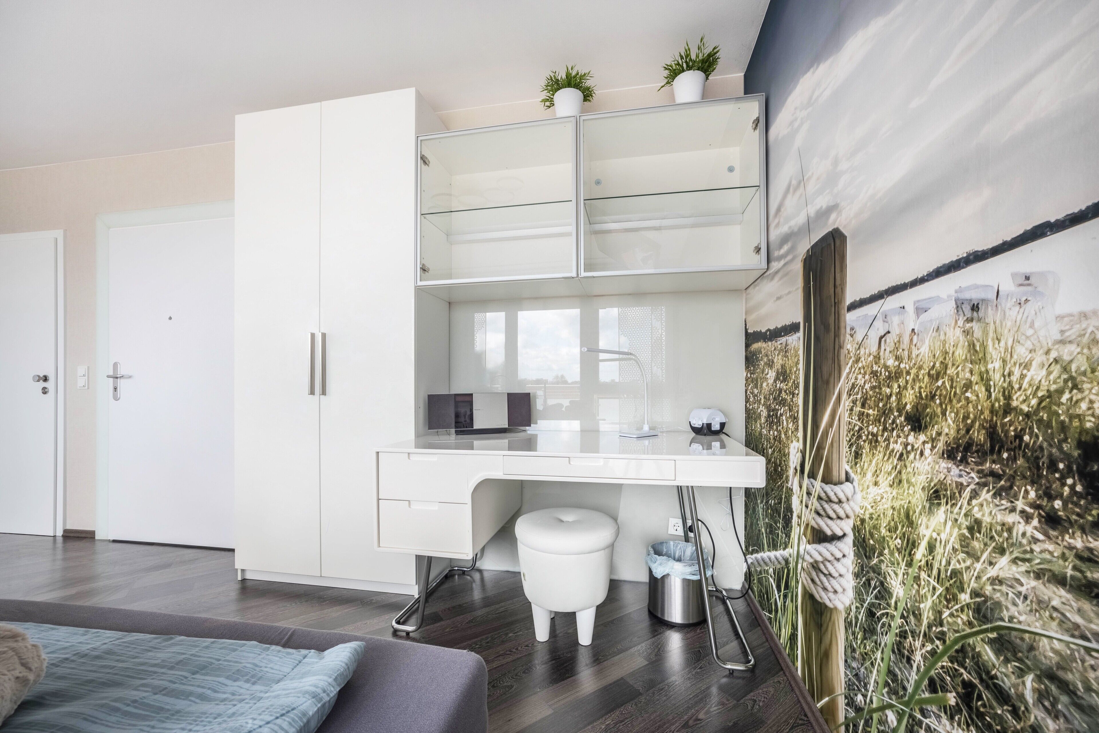 Ein modernes Schlafzimmer mit weißem Schreibtisch, weißem Kleiderschrank und einem großen Fenster.