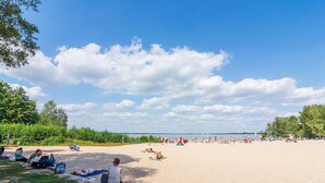 A beach with people sunbathing and sitting on the sand, a clear sky, and a calm sea in the background.