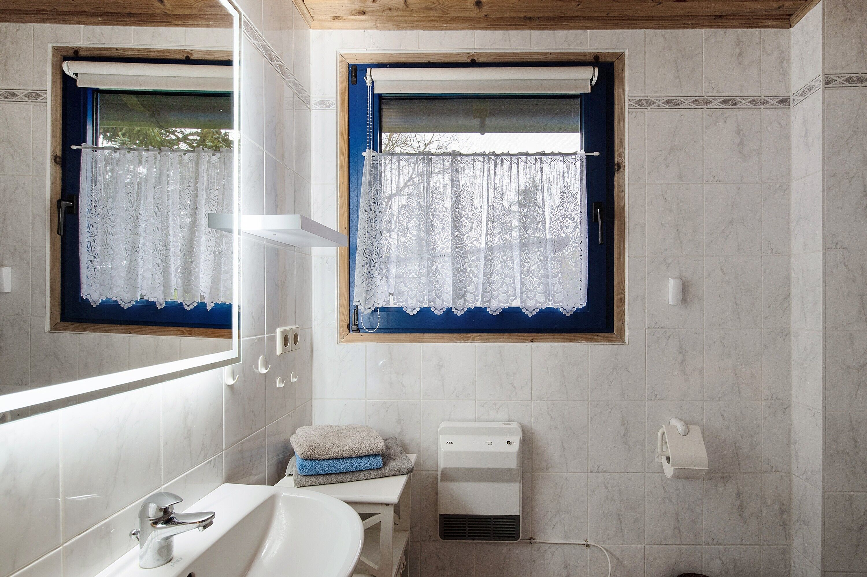 A bathroom with a white sink, a mirror, a window with a blue curtain, and a towel rack.