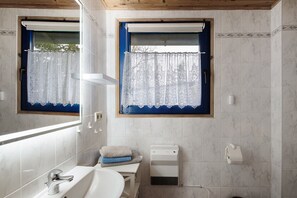 Un baño con un lavamanos blanco, un espejo, una ventana con cortina azul y un perchero para toallas.