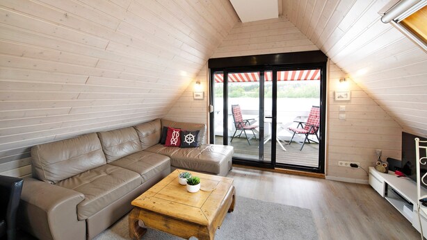 Ein gemütliches Zimmer mit Holzbalkendecke, einer Couch, einem Couchtisch und einer Schiebetür zu einem Sitzbereich im Freien.