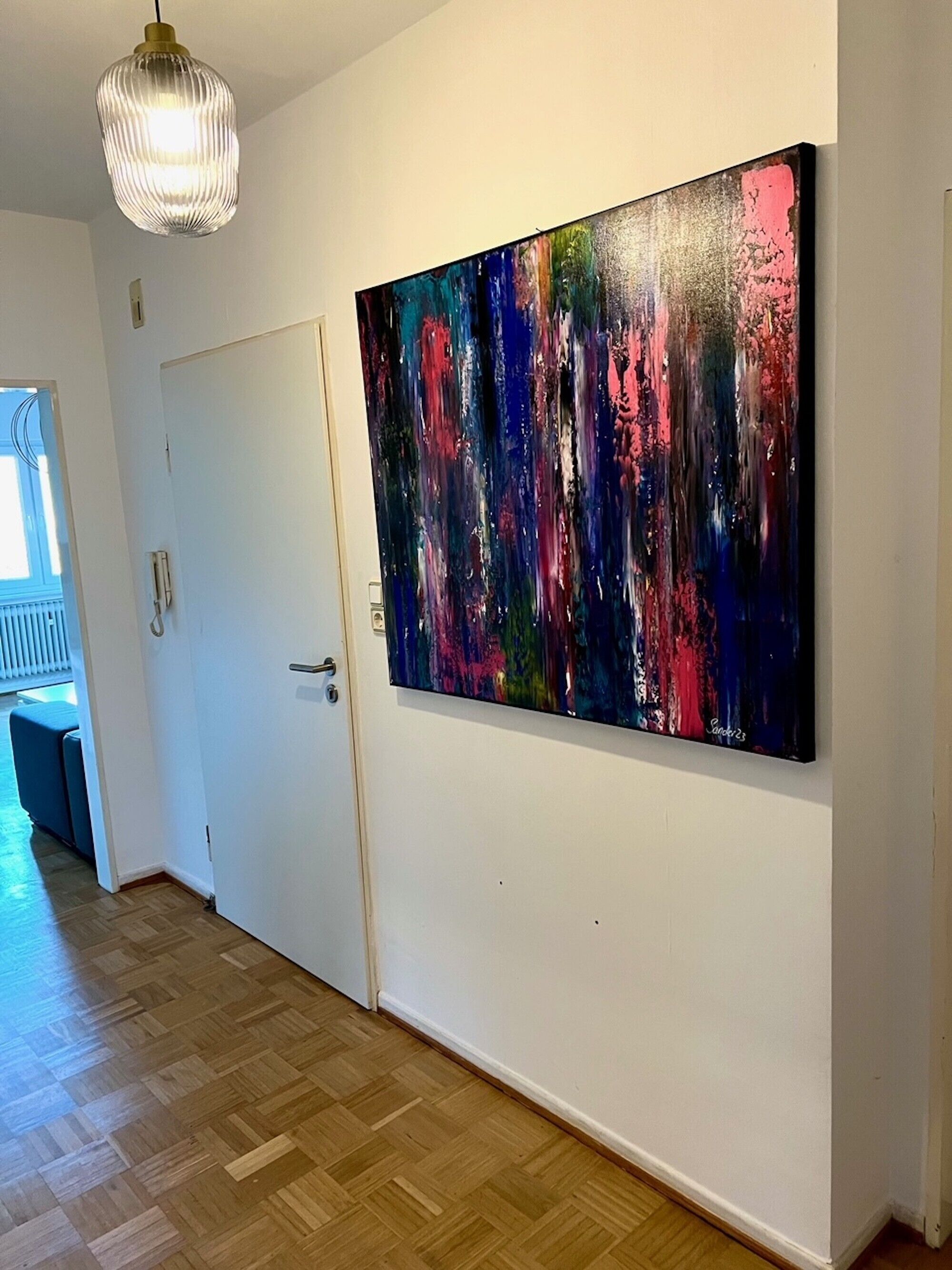 Ein Flur mit Holzboden, einer weißen Tür und einem großen abstrakten Gemälde an der Wand.