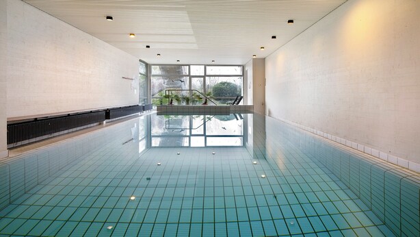 A large indoor swimming pool with a tiled floor, a glass railing, and a view of greenery outside. - Apartment 'Blackforest Perla' – Cozy Flat with Indoor Pool, Private Terrace, Fast Wi-Fi (Höchenschwand)