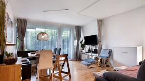 A modern living room with a dining area, a TV, and a comfortable seating arrangement. - Apartment 'Blackforest Perla' – Cozy Flat with Indoor Pool, Private Terrace, Fast Wi-Fi (Höchenschwand)