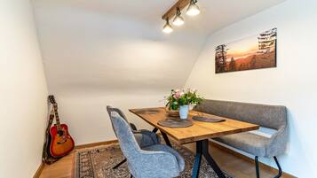 A dining area with a wooden table, grey upholstered bench, and a guitar against the wall.