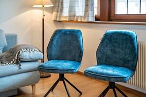Deux chaises bleues aux pieds noirs, dans une pièce où se trouvent une lampe, une fenêtre et un radiateur.