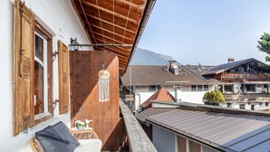 Een balkon met rieten meubilair, een houten wand en uitzicht op gebouwen en bergen.