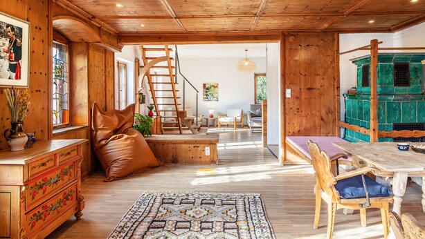 Een houten interieur met een trap, een eethoek en een uitzicht door een open deur.
