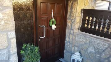 A stone wall, a wooden door with a metal handle, a wreath, a potted plant, and a white lantern.