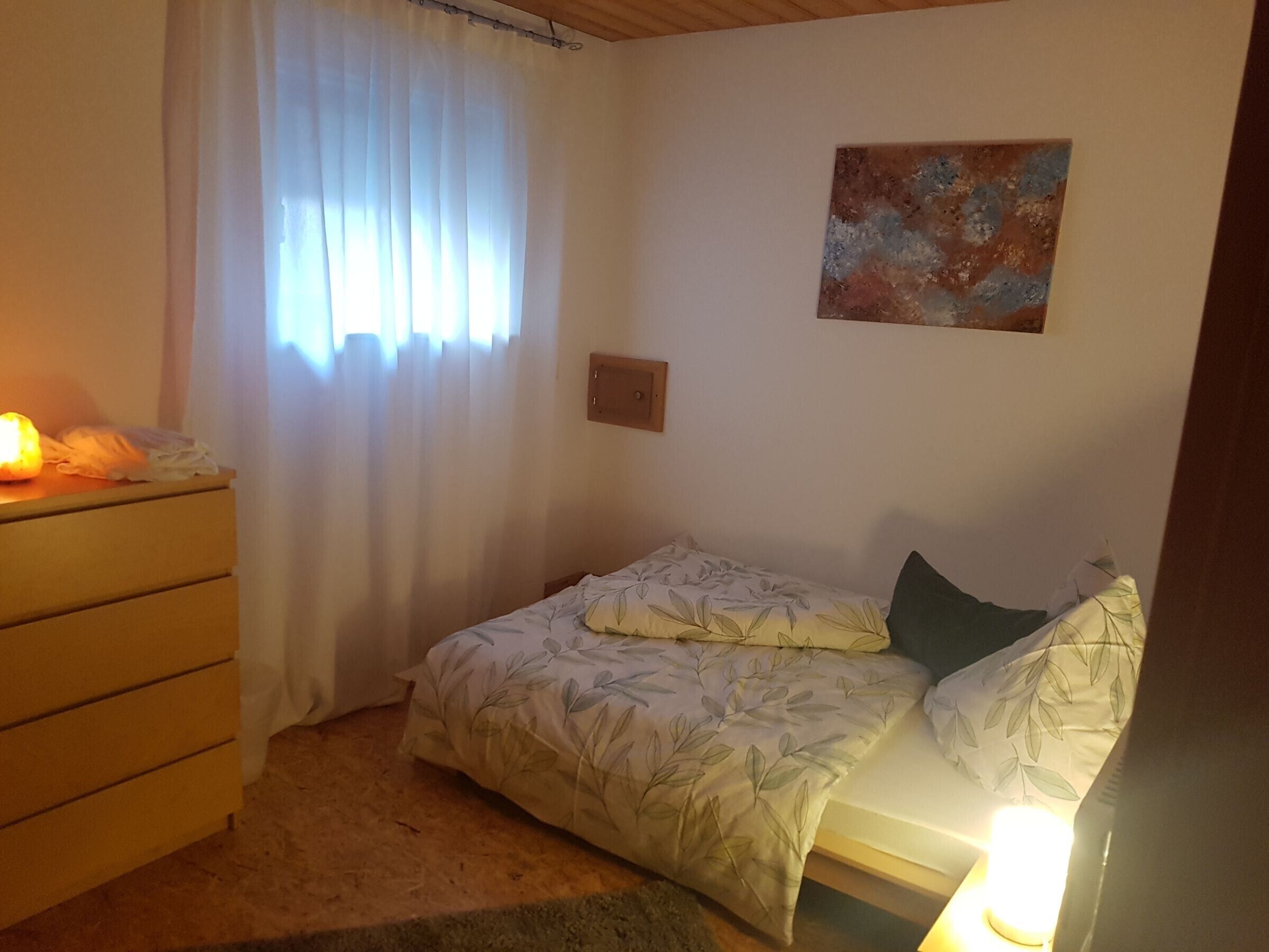 Ein Schlafzimmer mit einem Bett, einem Schminktisch, einem Nachttisch, einer Wandleuchte und einem Bild.