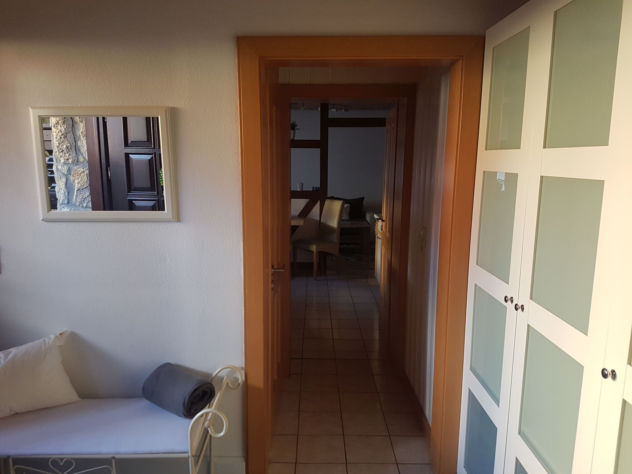 A hallway with a wooden door, a white wall with a framed picture, and a tiled floor.