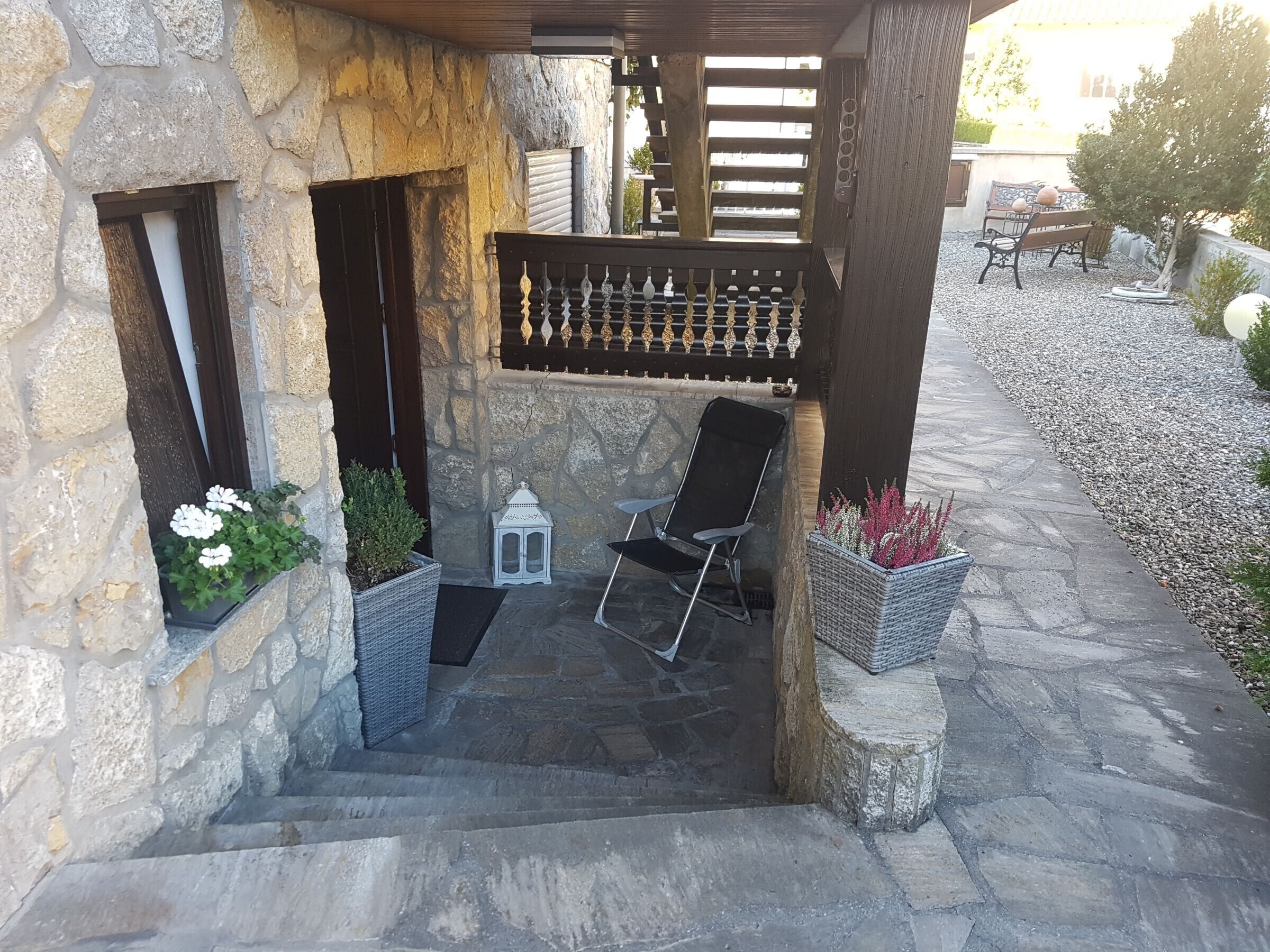 A stone building with a covered outdoor seating area, a chair, and potted plants.