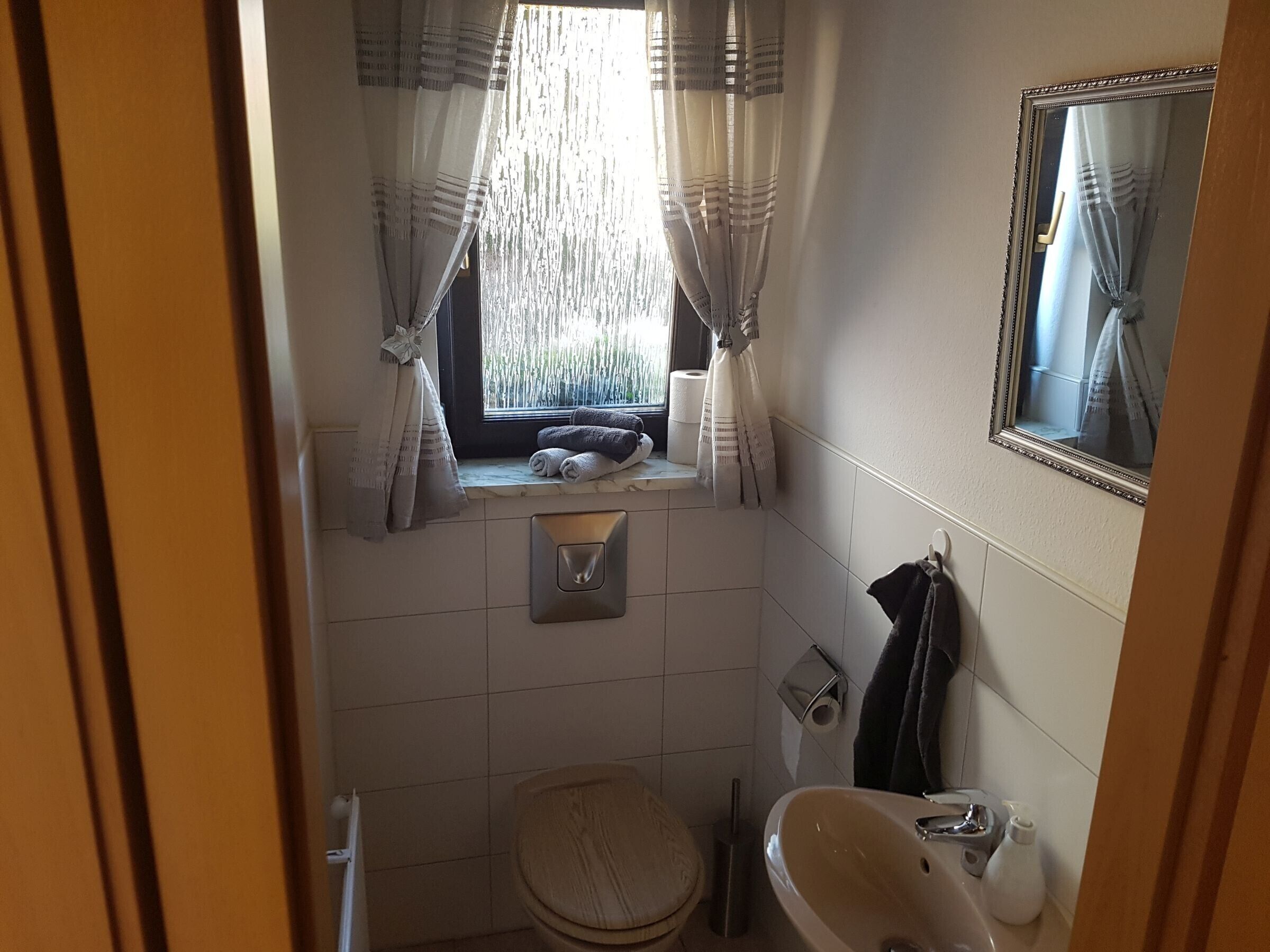 A small bathroom with a toilet, sink, and window with curtains.