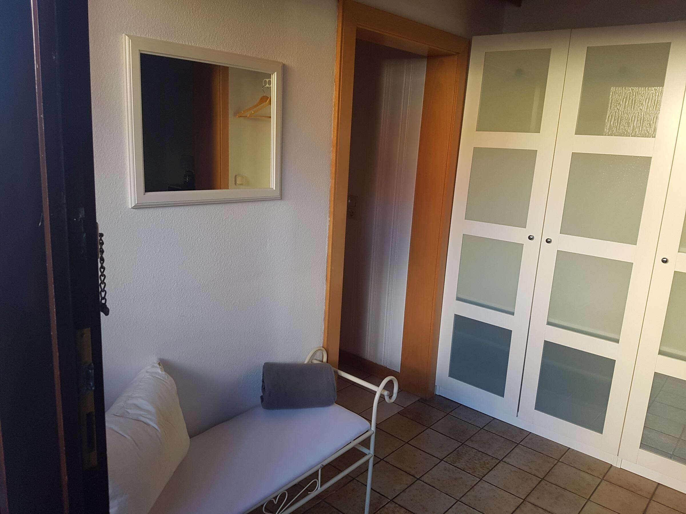A room with a white sofa, a mirror, a wardrobe with frosted glass doors, and a tiled floor.