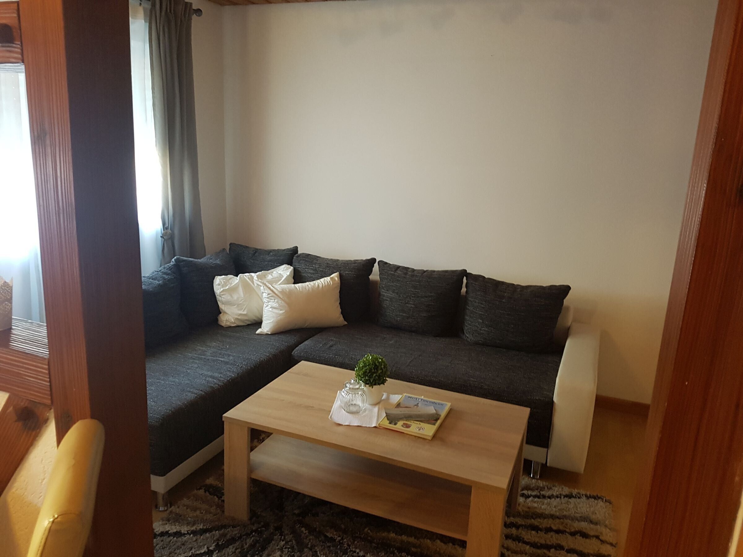 Una sala de estar con un sofá seccional gris oscuro, una mesa de centro de madera y una planta pequeña.