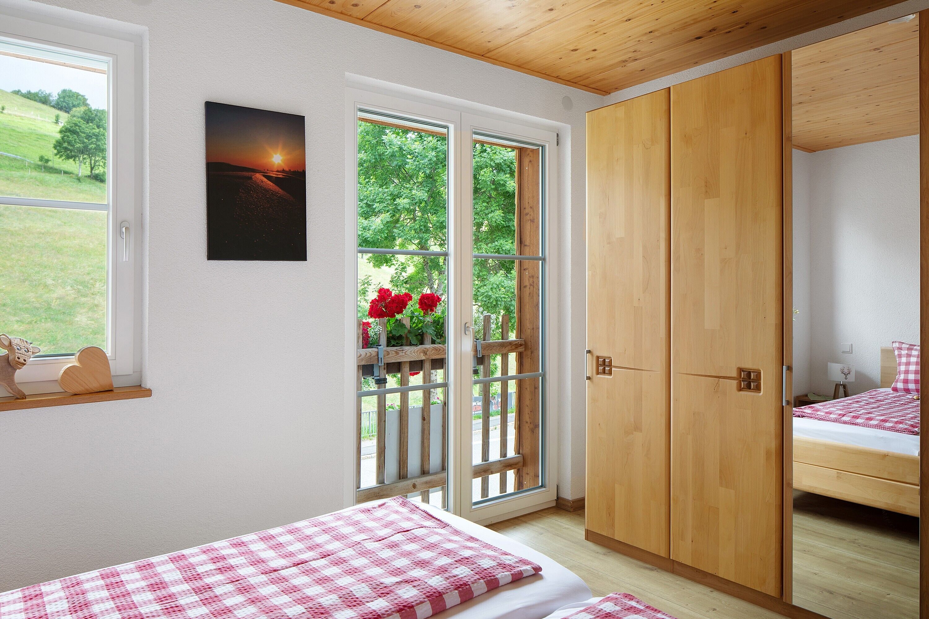 Ein Schlafzimmer mit einem Bett, einem Holzschrank, einem Fenster mit Blick ins Grüne und einem Bild an der Wand.