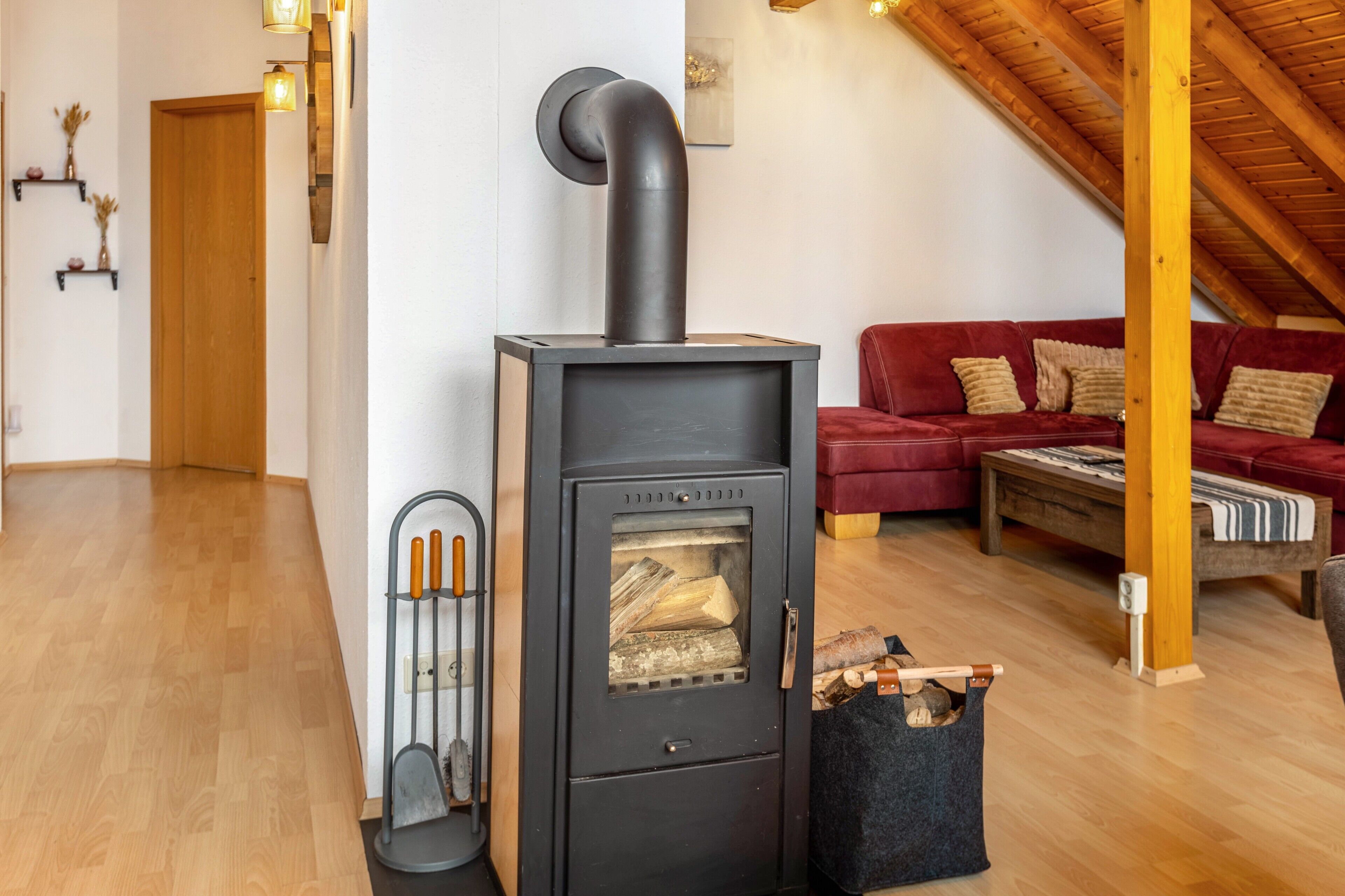 Een moderne woonkamer met een houtkachel, een rode bank en een houten plafond.