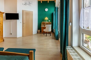 Une pièce avec un plancher en bois, un lit, un bureau avec une chaise, une télévision et une fenêtre avec des rideaux.