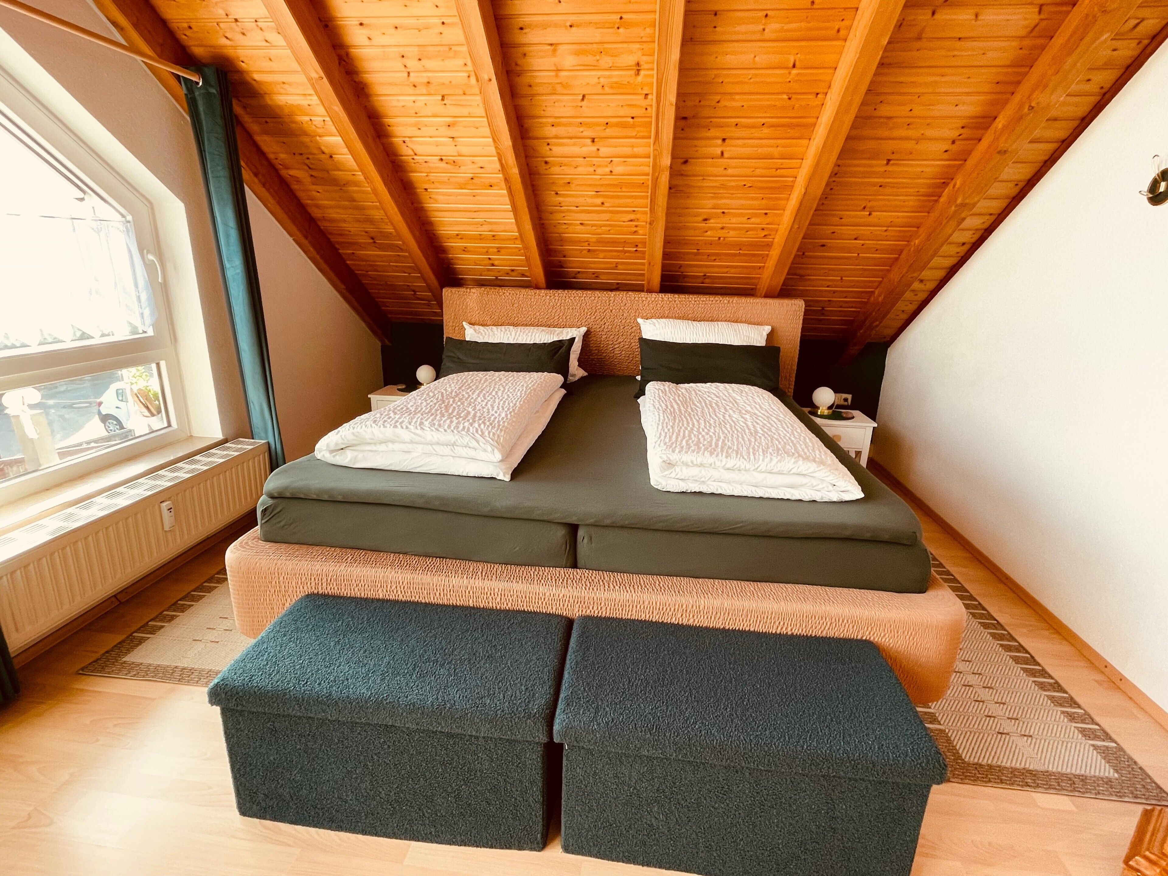 Una stanza con un letto, una finestra, un termosifone e un soffitto in legno.